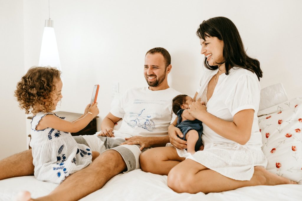 hombre, mujer con bebé e hija jugando con celular sobre la cama