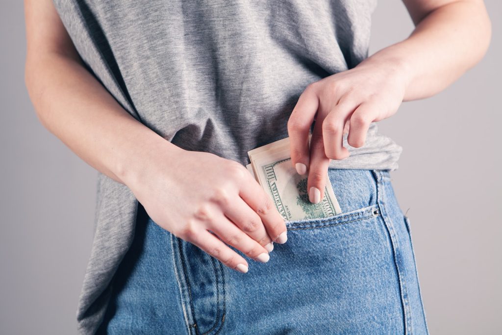 Persona con remera gris y jeans guardando plata en su bolsillo derecho
